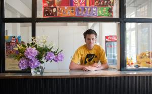 a man sitting at a counter with purple flowers at Ronneby Brunnspark Vandrarhem och B&B in Ronneby