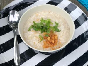 a bowl of oatmeal on a striped plate with a spoon at River Art Hotel in Chiang Mai