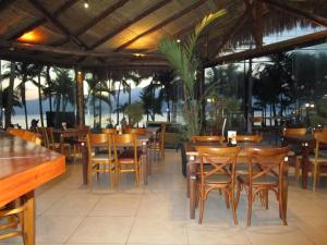 a restaurant with wooden tables and chairs and the ocean at Ilha Flat Hotel Suíte Bella - 4207 - Ilhabela in Ilhabela