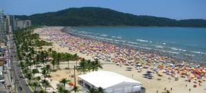 uma grande multidão de pessoas numa praia com guarda-sóis em Apartamento amplo com vista para o mar na Praia Grande na Praia Grande