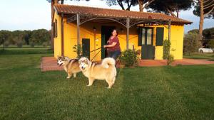 a woman standing in front of a yellow house with two dogs at La Fattoria di Tirrenia in Tirrenia