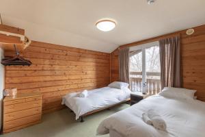 two beds in a room with wooden walls and a window at North Point in Niseko