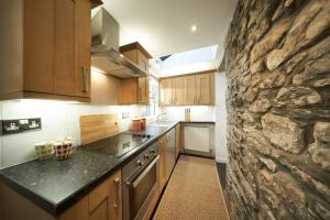 a kitchen with wooden cabinets and a stone wall at Stuc an t Sagairt Cottage , Loch Lomond in Drymen
