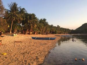 a beach with boats on the sand and palm trees at Seafront Cottage Ocam Ocam Beach in Busuanga