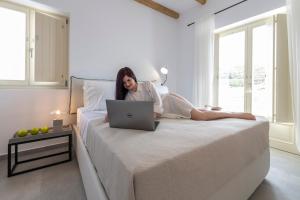 una mujer sentada en una cama con un portátil en Milos Zen Suites en Adamas