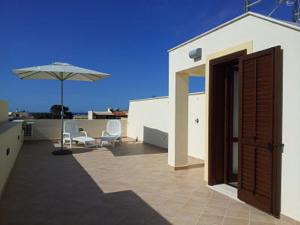 a patio with an open door and an umbrella at Essenzamare in San Vito lo Capo