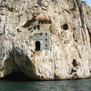 a building on the side of a rocky cliff at La Macchia Mediterranea in Bacu Abis