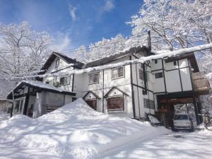 una casa coperta di neve con un mucchio di neve davanti di Hakuba Matata Lodge a Hakuba