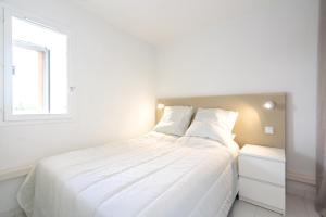 een wit bed in een witte slaapkamer met een raam bij Appart 6 pers vue mer-piscine-parking-clim-wifi in Cap d'Agde