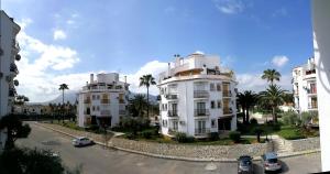 two white buildings next to a street with palm trees at Estudio con Piscina, Playa y Wifi in Denia