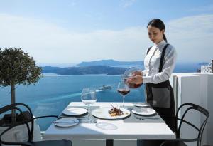 Eine Frau, die ein Glas Wein an einen Tisch gießt. in der Unterkunft Petit Palace Suites in Fira