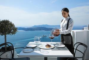 a woman pouring a glass of wine at a table at Petit Palace Suites in Fira