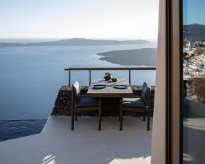 a table and chairs on a balcony with a view of the water at Vora in Imerovigli