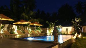 a swimming pool with chairs and umbrellas at night at Kayuna Villa in Nusa Penida