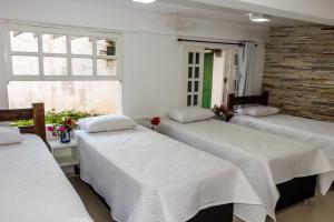Zimmer mit 3 Betten und weißer Bettwäsche in der Unterkunft Pousada Paraiso do Alto in Paraisópolis