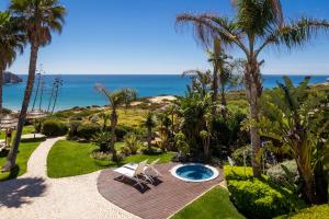 um jardim com uma banheira de hidromassagem, palmeiras e o oceano em Mareta View - Boutique Bed & Breakfast em Sagres