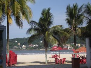 una playa con sillas, sombrillas y palmeras en Apartamento Temporada, en São Vicente