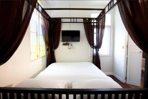 a bed in a bedroom with curtains and a tv at 99 Oldtown Boutique Guesthouse SHA EXTRA PLUS in Phuket Town