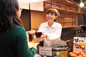 a woman standing in a kitchen holding a plate of food at Matsumoto Tourist Hotel in Matsumoto