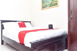 1 dormitorio con 1 cama con sábanas blancas y almohadas rojas en RedDoorz Syariah near Gelora Delta Sidoarjo 2, en Sidoarjo