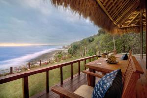 Lelewatu Resort Sumba في Watukarere: شرفة مع طاولة وكراسي والمحيط