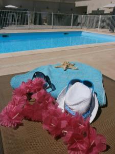 a hat and sunglasses and pink flowers next to a swimming pool at Résidence Thalacap in Cap d'Agde