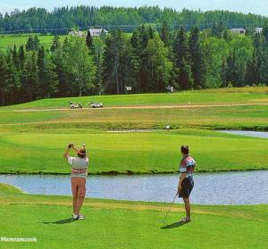 two people standing on a golf course near a body of water at Cottage Jasmine on the Shediac Bay with hot tub in Shediac