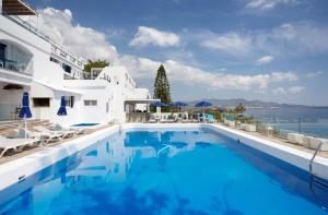 a swimming pool with white buildings and the ocean at Karma Minoan in Agios Nikolaos