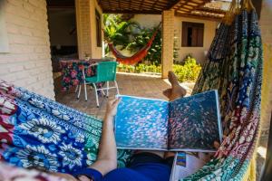 a person laying on a hammock reading a book at Pousada Cores dos Corais in Maracajaú