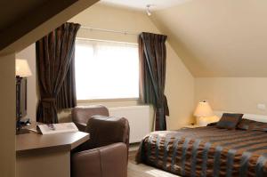 a bedroom with a bed and a chair and a window at Hotel Salons De Vrede in Ichtegem