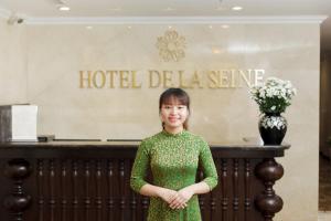 een vrouw in een groene jurk die voor een hotel delia bord staat bij Hotel De La Seine in Hanoi