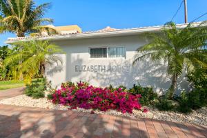 Um edifício branco com flores cor-de-rosa à frente. em Elizabeth House Inn em Deerfield Beach