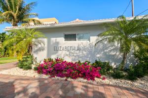 Un edificio blanco con flores rosas delante. en Elizabeth House Inn, en Deerfield Beach
