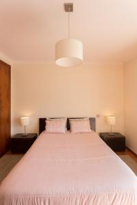 サン・マルティーニョ・ド・ポルトにあるApartamento Praia São Martinho do Portoのベッドルーム1室(ピンクのシーツとランプ2つ付きの大型ベッド1台付)