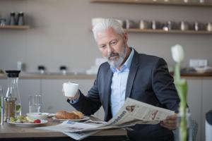 un hombre sentado en una mesa con un periódico y una taza de café en TT Aparthotel Neuhofen en Neuhofen an der Krems