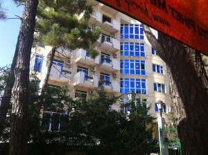 a building with blue windows in front of some trees at Hotel Kamomil in Durrës