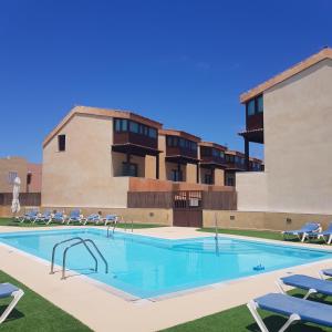 a swimming pool with chairs and a building at VILLA 16 LUJO A 200 M DEL MAR in Corralejo