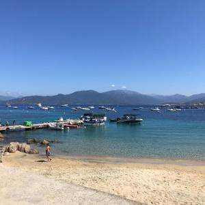 a person walking on a beach with boats in the water at HOTEL CAMPOMORO in Belvédère-Campomoro