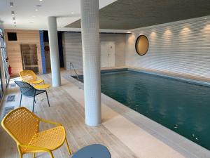 a swimming pool in a building with chairs and a table at DOMITYS - Les Safrans in Dives-sur-Mer