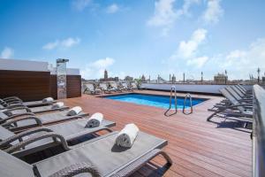 a deck with chairs and a swimming pool on a roof at Salles Hotel Málaga Centro in Málaga