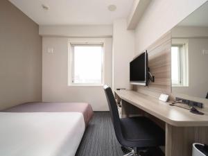 a hotel room with a bed and a desk with a television at Super Hotel Yokohama Kannai in Yokohama