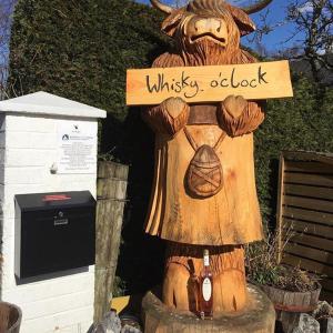 a wooden statue of a cow holding a whiskey adviser sign at Ardlogie Guest House in Aviemore