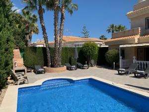 a swimming pool in front of a house with palm trees at 17 Vistamar Playa Flamenca in Playa Flamenca