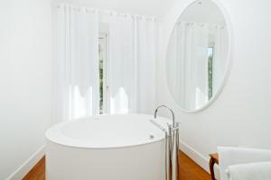 a white bathroom with a round mirror and a tub at Bellevue Syrene in Sorrento