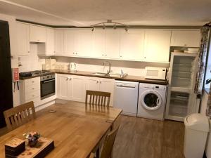 uma cozinha com armários brancos, uma mesa e uma máquina de lavar louça em Linhay -Farm Cottage em Sidmouth