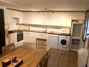 a kitchen with white cabinets and a table and a dishwasher at Linhay -Farm Cottage in Sidmouth