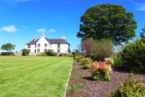 a white house with a tree and some flowers at Tarrel Farmhouse in Portmahomack