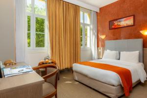 um quarto de hotel com uma cama, uma secretária e janelas em Kyriad Avignon - Palais des Papes em Avignon