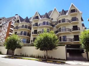 um grande edifício de apartamentos branco com árvores em frente em Apto Deslumbrante em Capivari proximo a BADEN BADEN em Campos de Jordão