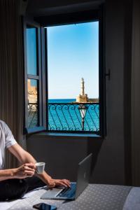 eine Person, die auf einem Bett mit einem Laptop und einem Fenster sitzt in der Unterkunft Elia Zampeliou Hotel in Chania